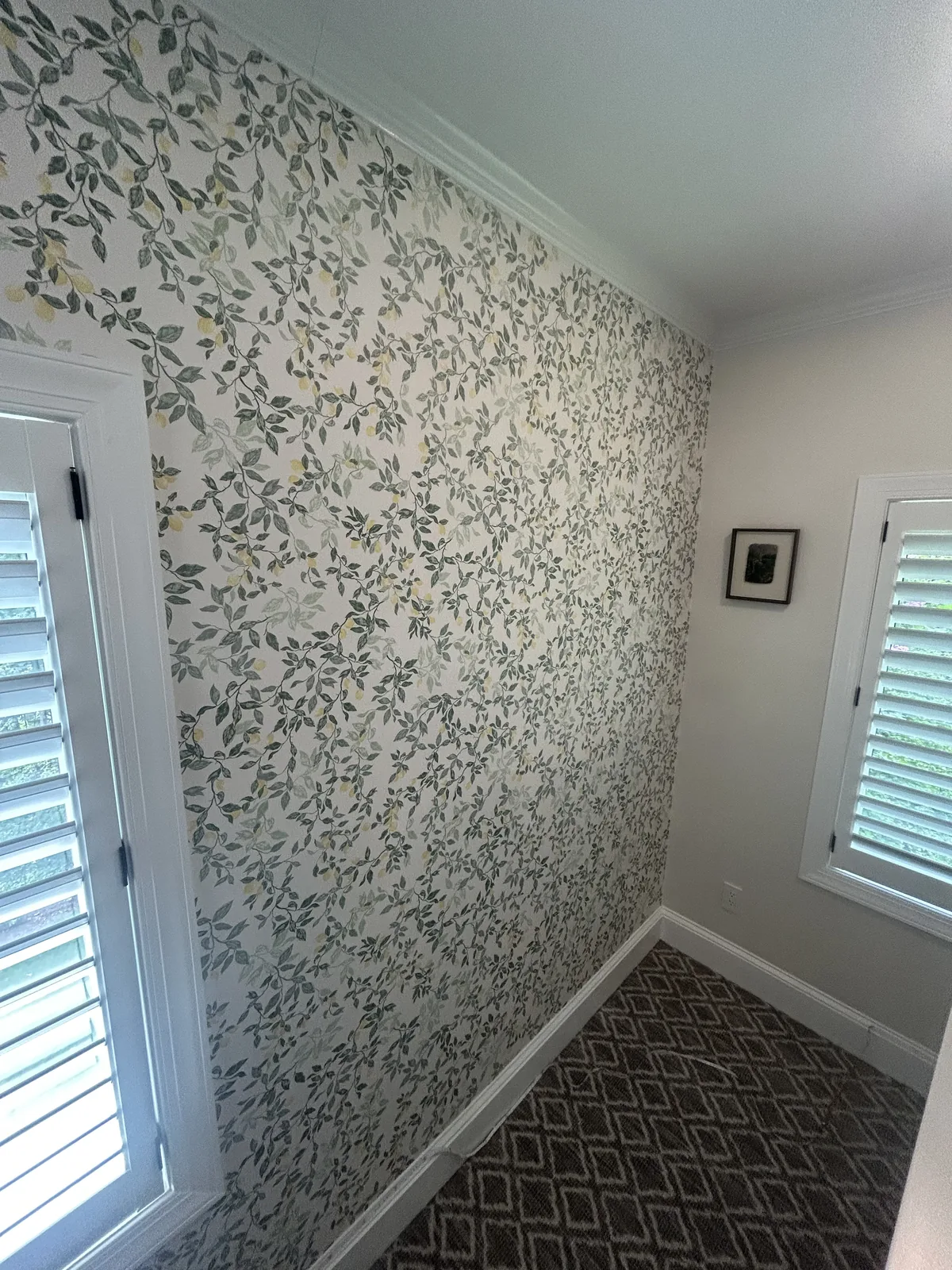 Coastal botanical wallpaper installation in sunroom with plantation shutters and sisal geometric floor