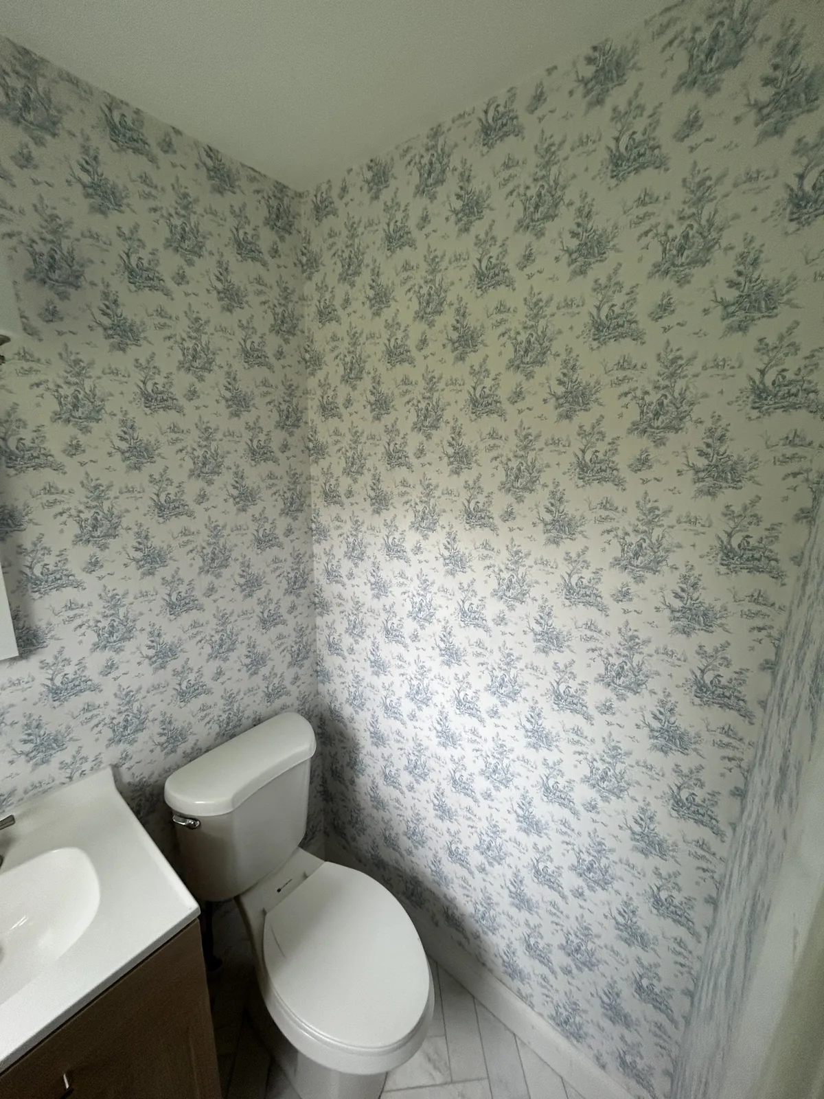 French Toile de Jouy wallpaper installation in Hamptons estate powder room with herringbone marble floor