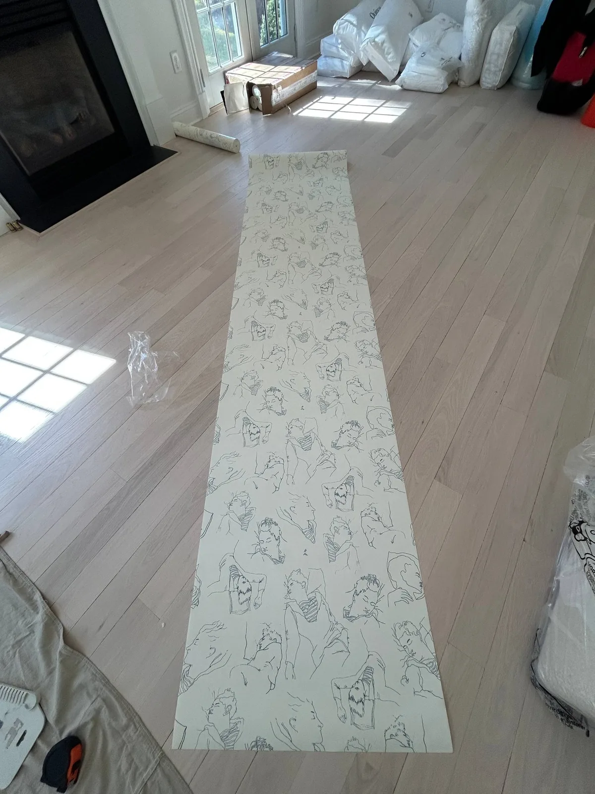 Master artisan laying out designer wallpaper rolls on white oak floors before paste application